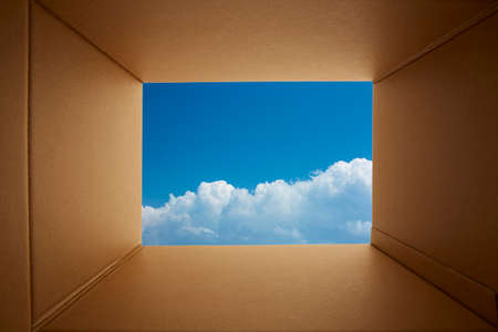 Looking though cardboard open box toward blue sky background.の写真素材