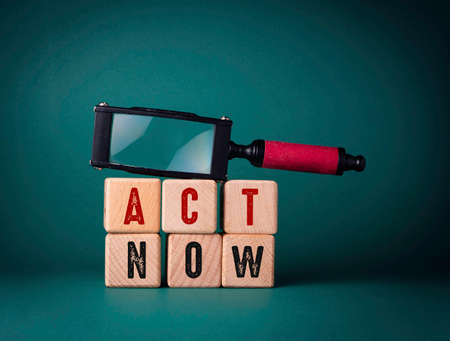 The word Act now is written on wooden cubes on a green background.の写真素材