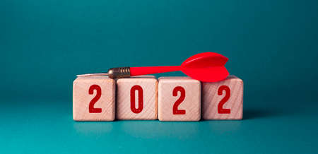 2022 new year concept. Red dart on wooden cubes with numbers 2022 on green background.