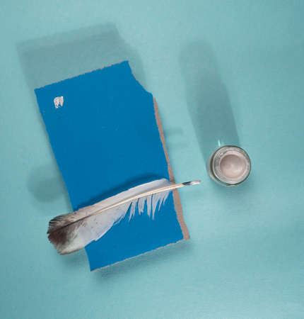A piece of paper with a feather and a candle on a blue backgroundの写真素材