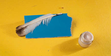 white feather and a blank blue sheet of paper on a yellow backgroundの写真素材