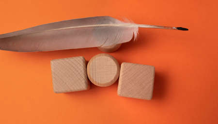 Wooden cubes and feather on orange background, flat lay. Space for textの写真素材