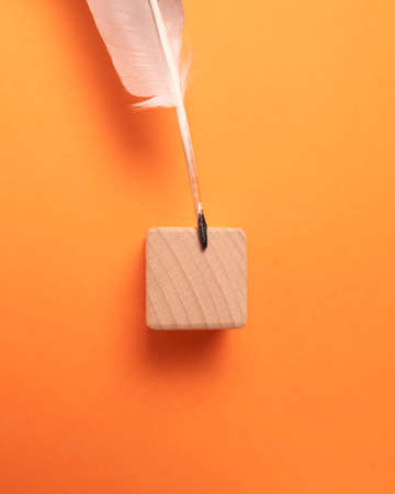 White quill and wooden cube on orange background, top view. Space for textの写真素材