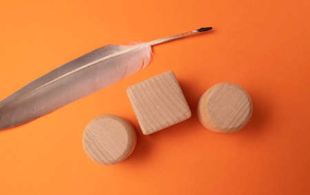 Wooden cubes with feather on orange background, flat lay. Space for textの写真素材