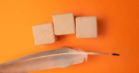 Wooden cubes with feather on orange background, flat lay. Space for textの写真素材