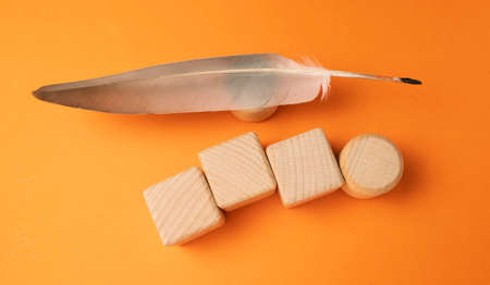 wooden cubes with feather on orange background, top view, flat layの写真素材