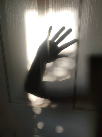 Whisper of Light. A mysterious and artistic image capturing the shadow of a hand on a textured glass door, illuminated by soft natural light.の写真素材