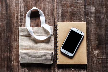 Smartphone on notebook and calico bags on old wooden tableの写真素材