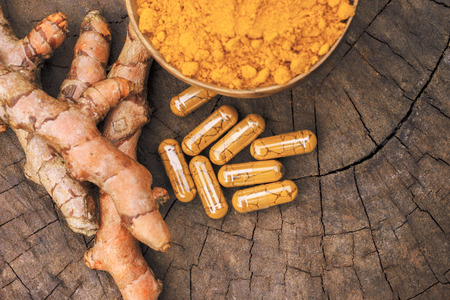 Turmeric powder in wooden bowls and turmeric capsules on wooden backgroundの写真素材