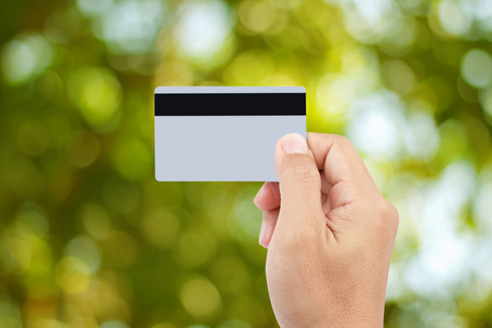 Man hand holding credit or debit card  on abstract green bokeh background for credit card payment...