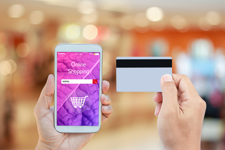 Hand holding smart phone with online shopping on screen and credit card over blurred in shopping mall background for mobile banking payment online conceptの写真素材
