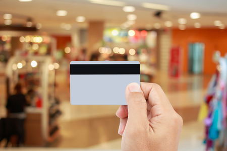 Man hand holding credit card on blur of shopping mall with shining bokeh lights for credit card payment conceptの写真素材