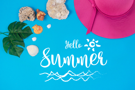 Hello Summer text on blue background, Pink hat with green tropical palm leaf and shell. Beach accessoriesの写真素材