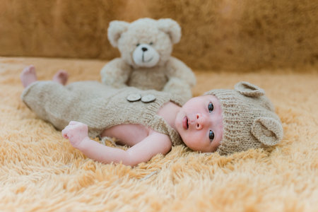 Portrait of twenty seven day old asian baby boy in knitted bear suit with hat and teddy bear sleeping on brown fur bed in the studioの写真素材