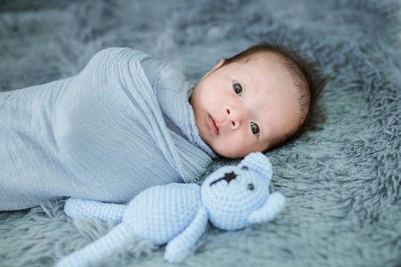 Portrait of twenty seven day old newborn asian baby boy in blue swaddling with teddy bear sleeping...