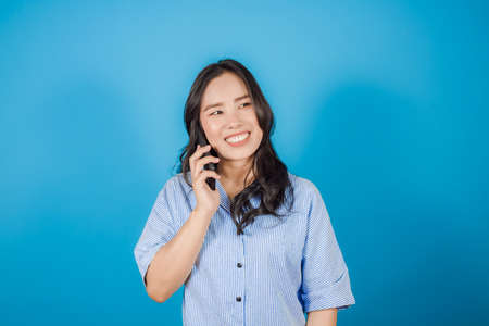 Portrait of happy excited Asian woman having conversation talking on the smartphone on light blue backgroundの写真素材