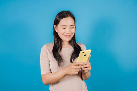 Portrait of smiling Asian woman wears nude t-shirt using a smartphone isolated on blue background