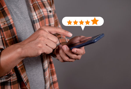 Customer service experience and business satisfaction survey. Man hand using smartphone with popup five star icon for feedback reviewの写真素材