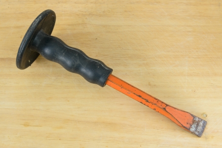 Old rusty chisel with black rubber handle on wooden table 