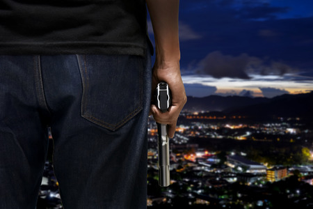 A man hold and resting firearm beside body rear view with blurred city background