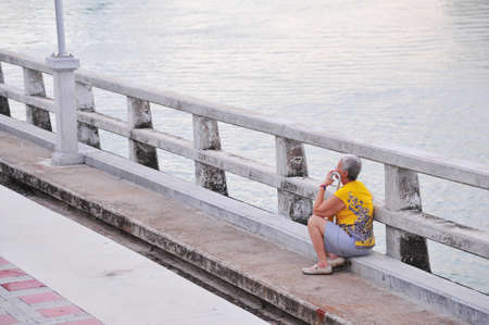old asian lady resting on concrete bridgeの写真素材