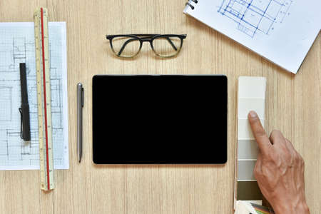 a top view of architect working desk with hand work point to color chart with equipments for drawings sketched on wood table, the concept of modern technology for architectural working with tabletの写真素材