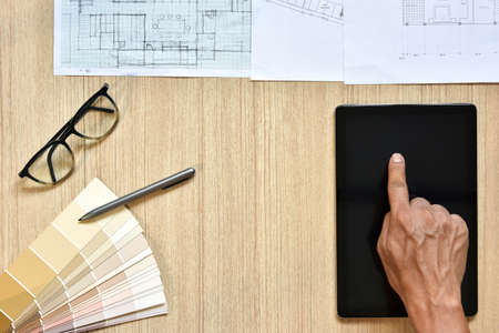 a top view of architect working desk with hand touch on equipments for drawings pens sketched idea on wood table, the concept of modern technology for architectural working with tabletの写真素材