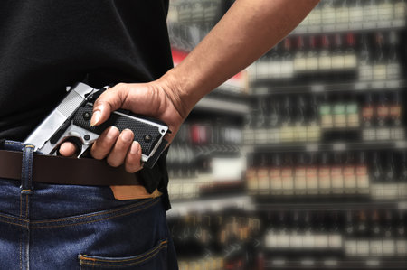 A man pulls out a gun tucked in his pant rear view with blurred department store background, a...