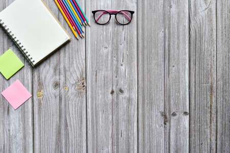 Still life, business office supplies or education concept, Top view image of open notebook and various colorful pencil and eyeglasses with blank pages on old brown wooden, ready for adding textの写真素材