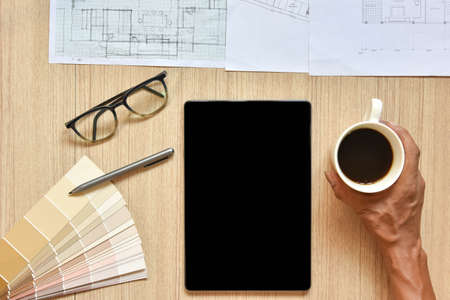 a top view of architect working desk with hand hold coffee cup with equipment for drawings pens...