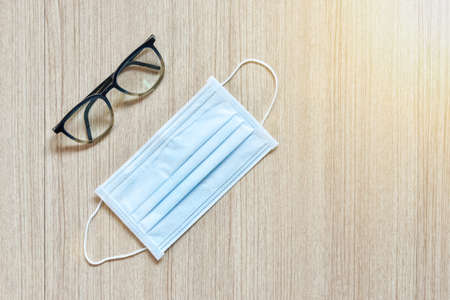 Clear eyeglasses and protection mask, Glasses transparent dark blue frame with protection paper mask on a wooden background, a concept of virus and pollution protection with copy spaceの写真素材