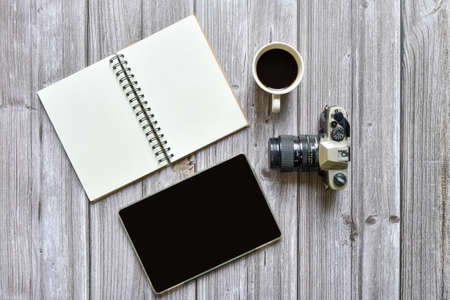 Still life, business or traveler memo concept, Top view image of open notebook with vintage camera coffee and tablet with blank pages on old brown wooden background, for adding textの写真素材