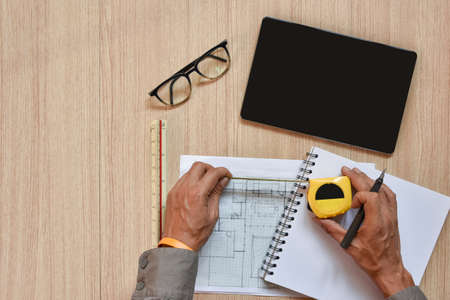 a top view of architect working desk with hand work on measurement tape for drawings pens sketched...