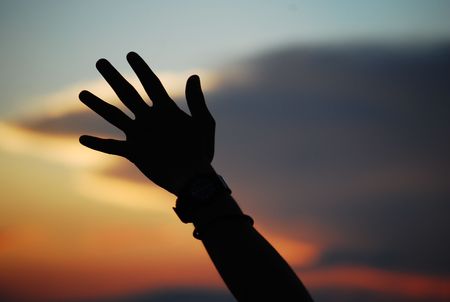 Hand raised toward the sky at duskの写真素材