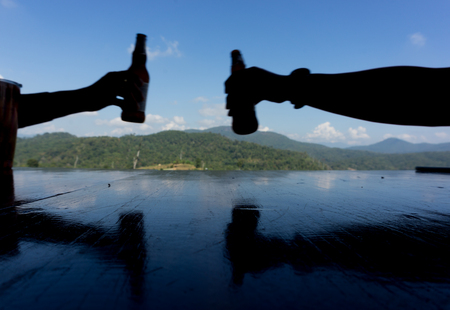 Two hands holding beer bottles and clinking on blue background.の写真素材