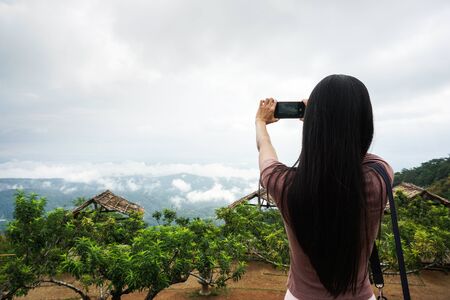Woman taking photo with smart phone, view of blue sky at Mon Cham, Chiang Mai, Thailand.の写真素材