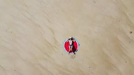 Woman wearing sun hat at the beach and lying on a white sand, Top view from flying drone.