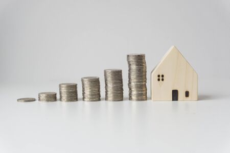 White wooden houses with silver coins stacked in order of height, white background, business idea, business growth.の写真素材