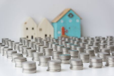 Silver coins are stacked in a row and the 3 small houses are at the back. Concept of saving money to buy a house in the future.の写真素材