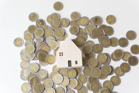 White wooden house placed on a silver coin that was scattered on the ground, White background, business idea.の写真素材