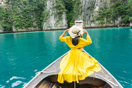Beautiful woman in bright yellow dress, wearing hat with a black bow, on local long tail boat of...