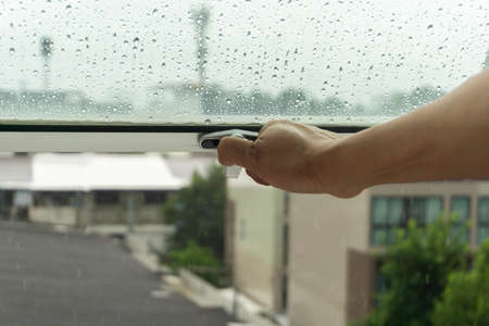 The woman's hand was closing the window because of the rain.