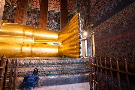 woman cleaning a big buddha gold statue at Wat Pho, Bangkok, Thailand.のeditorial素材