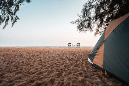 Tent under pine trees, chairs and camping table on the sand in front of the tent, camping at the...