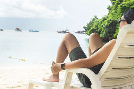Male Asian tourists lie on beach chairs, sea views, and Thai long-tailed boats.の写真素材