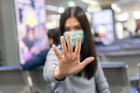 Asian woman wearing a surgical mask to protect against coronavirus, Lady sitting at Bangkok International Airport and show stop hands gesture.の写真素材