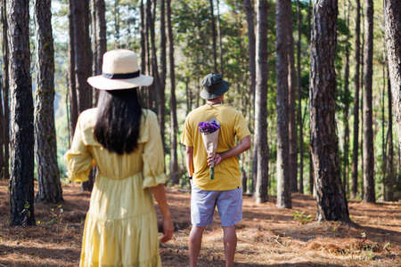 A man in a yellow shirt holds a bouquet of flowers behind it and a woman in a yellow dress stands behind a man, a surprise couple concept.の写真素材