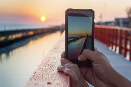 Man taking picture of the sunset with mobile phone.の写真素材