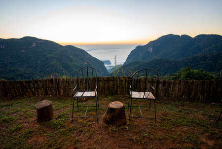 2 wooden chairs with mountains, clouds and sky with beautiful morning sunrise.の写真素材