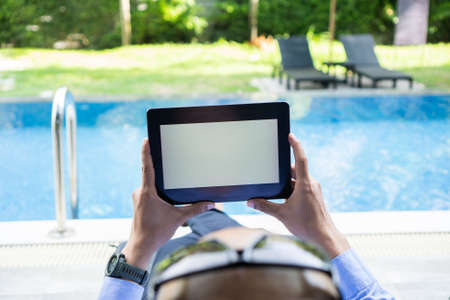Business man holds tablet with isolated screen in his hands, blank white screen at swimming pool.の写真素材